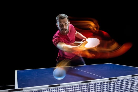 The table tennis player in motion. Fit young sports man tennis-player in play on black background with lights. Movement, sport game, stobe concepts. Professional. Human emotions, facial expression