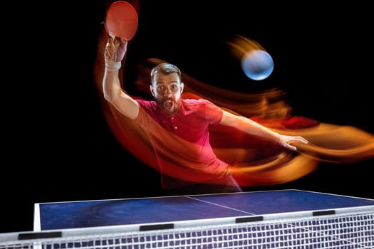 The table tennis player in motion. Fit young sports man tennis-player in play on black background with lights. Movement, sport game, stobe concepts. Professional. Human emotions, facial expression