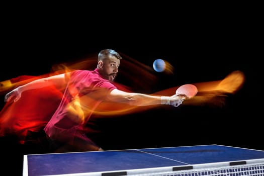 The table tennis player in motion. Fit young sports man tennis-player in play on black background with lights. Movement, sport game, stobe concepts. Professional. Human emotions, facial expression