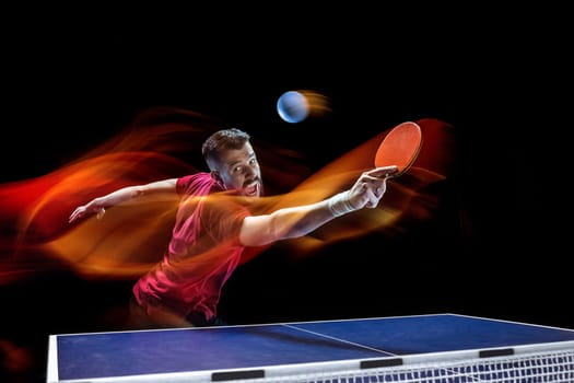 The table tennis player in motion. Fit young sports man tennis-player in play on black background with lights. Movement, sport game, stobe concepts. Professional. Human emotions, facial expression