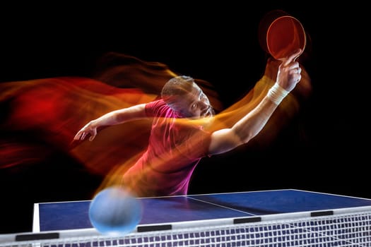 The table tennis player in motion. Fit young sports man tennis-player in play on black background with lights. Movement, sport game, stobe concepts. Professional. Human emotions, facial expression