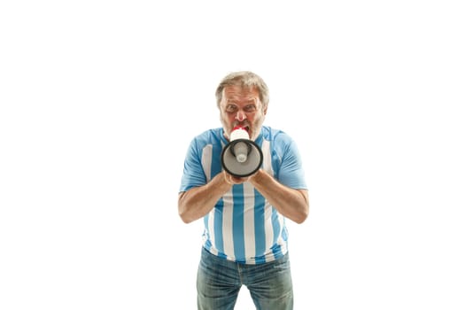 The senior Argentinean fan celebrating on white background. The mature man in soccer football uniform screaming in megaphone isolated at white studio. Fan, support concept. Human emotions concept.