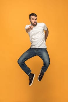 Freedom in moving. Mid-air shot of handsome happy young man jumping and gesturing against orange studio background. Runnin guy in motion or movement. Human emotions and facial expressions concept