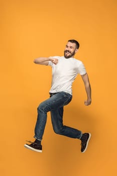 Freedom in moving. Mid-air shot of handsome happy young man jumping and gesturing against orange studio background. Runnin guy in motion or movement. Human emotions and facial expressions concept
