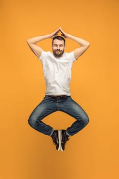 Freedom in moving. Mid-air shot of handsome happy young man jumping and gesturing against orange studio background. Runnin guy in motion or movement. Human emotions and facial expressions concept
