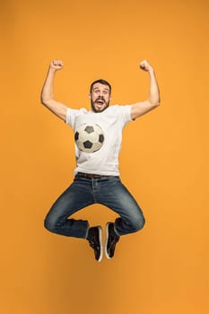 Forward to the victory.The young man as soccer football player jumping and kicking the ball at studio on a yellow background. Football fan and world championship concept. Human emotions concepts