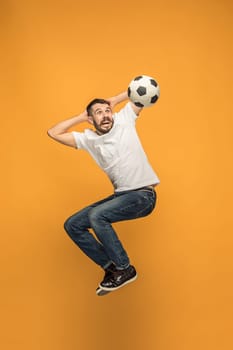 Forward to the victory.The young man as soccer football player jumping and kicking the ball at studio on a yellow background. Football fan and world championship concept. Human emotions concepts