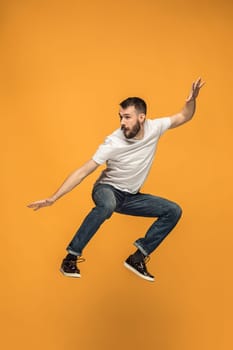 Freedom in moving. Mid-air shot of handsome happy young man jumping and gesturing against orange studio background. Runnin guy in motion or movement. Human emotions and facial expressions concept