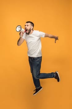 Soccer fan jumping on orange background. The young man as football fan with megaphone isolated on orange studio. Support concept. Human emotions, facial expression concepts.