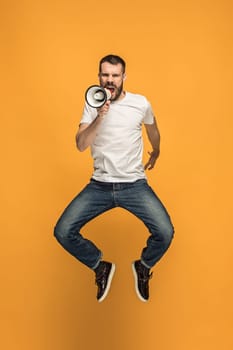 Soccer fan jumping on orange background. The young man as football fan with megaphone isolated on orange studio. Support concept. Human emotions, facial expression concepts.
