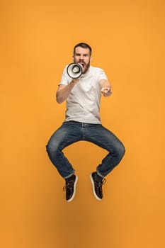 Soccer fan jumping on orange background. The young man as football fan with megaphone isolated on orange studio. Support concept. Human emotions, facial expression concepts.