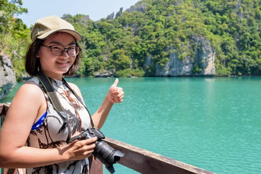 Woman tourist at Thale Nai holding dslr camera and thumbs up after taking pictures of Blue Lagoon (Emerald Lake) on Koh Mae Ko island viewpoint in Mu Ko Ang Thong National Park, Surat Thani, Thailand