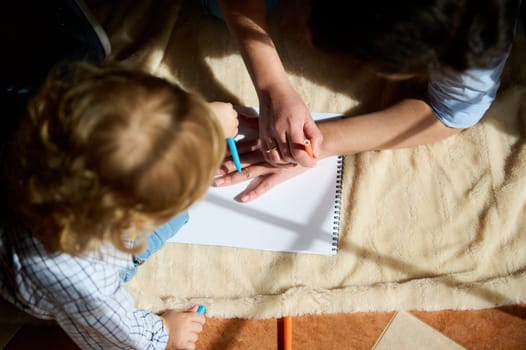 A mother helps her child draw on a sheet of paper while enjoying quality time together, fostering creativity and their warm bond.