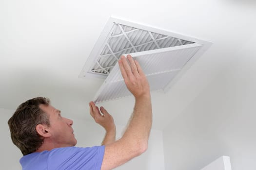 Man shutting grill of HVAC, heating ventilating and cooling after replacing the air filter. Closing ceiling grill after replacing an air filter in the ceiling.