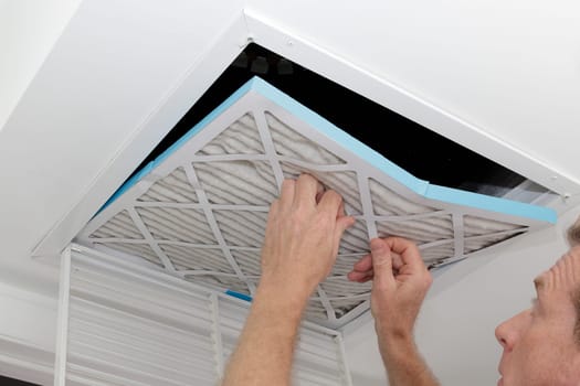 Person removing an old dirty air filter from a ceiling intake vent of a home HVAC system. Unclean gray square furnace air filter being taken out of a ceiling air vent.