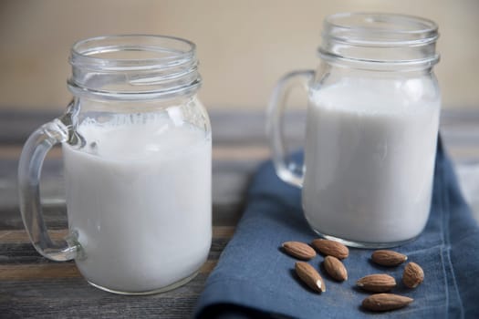 two jars of almond milk with raw almonds on rustic wooden table with blue napkin.