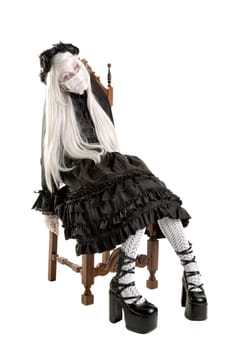 Girl in a black dress with white eyes looking like a doll in a chair isolated in white