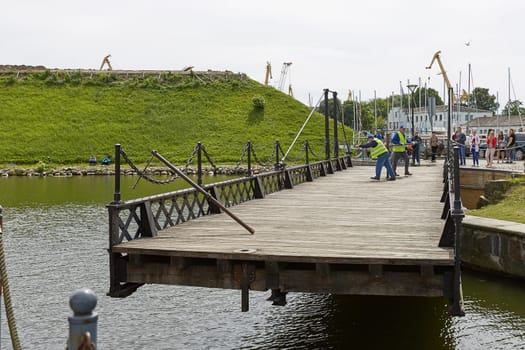 KLAIPEDA, LITHUANIA - JULY 05, 2017: Unidentified workers perform manually turn of wrought Swing bridge built in 1855 in Castle port of Klaipeda across moat Dassel between Castle Pond and river Dange. It is only mechanism of its type in Baltic countries
