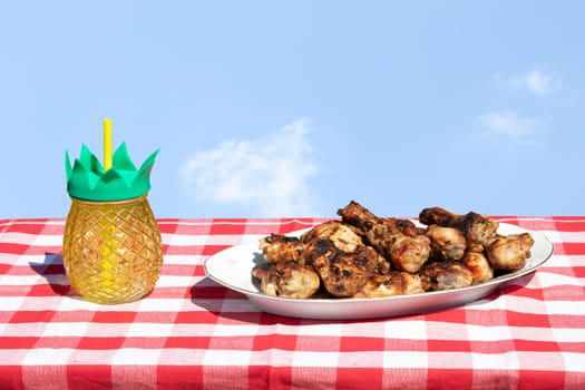 Fresh grilled chicken meat and a glass of juice on table with bright sky.