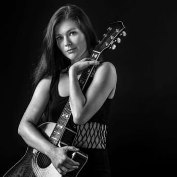 Photo of a young beautiful woman holding an acoustic guitar.