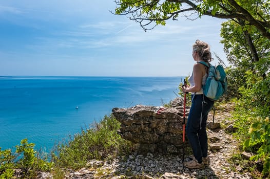 Mature hiker female with backpack looking forward on sea, sky. Travel and active lifestyle concept. Trieste,Italy.