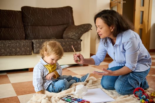 A caring mother engages with her young child in an artistic activity with paints, fostering creativity and strong emotional connection in a warm home environment.