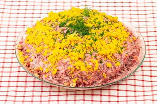 Traditional russian layered salad named herring under a fur coat. Traditional Russian cuisine presented at red checkered tablecloth. Concept Russian food.