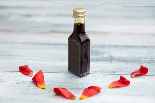 Bottle with oil and fresh tulips pedals on bright rustic wooden table with text copy space.
