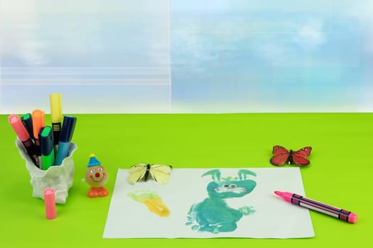 Happy childrens day. Workplace from child is painting his mother a bunny picture and some toys over bright blue background. Space for your design.