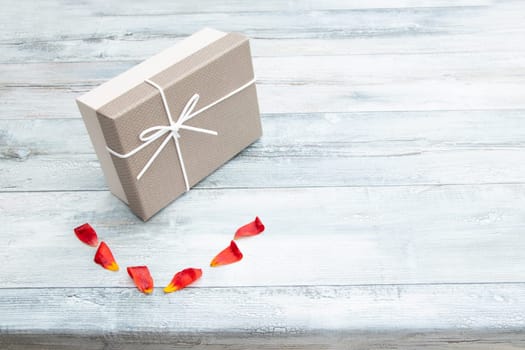 Gift box and  tulips petals with place for your text on rustic bright wooden table. Card concept.