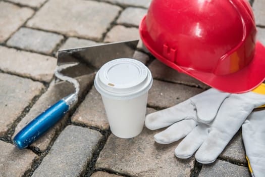 red helmet, trowel,coffee mug and work gloves on stones