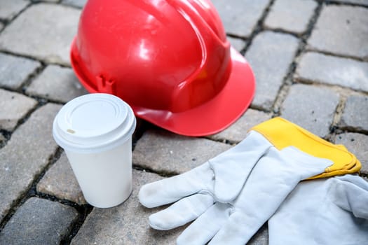 red helmet,coffee mug and work gloves on stones