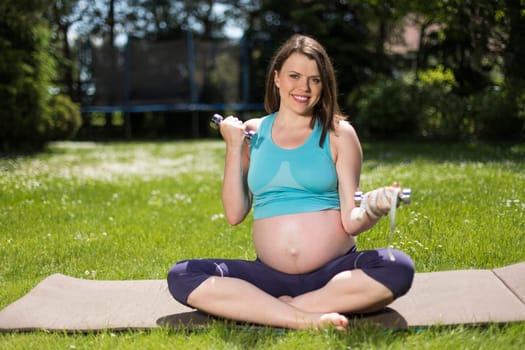 Pregnant woman doing fitness exercise on the grass