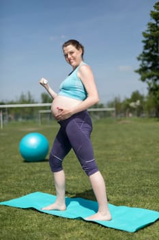 Pregnant woman doing fitness exercise on the grass