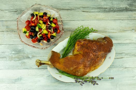 A roast turkey leg or drumstick and a glas bowl with fresh spring salad on rustic wooden bright table. After cooking. Concept food.
