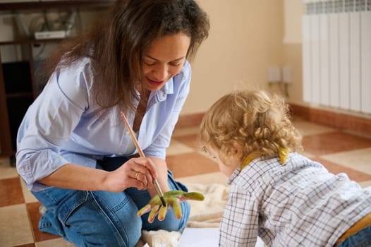 A loving moment of a mother painting her child's hand, emphasizing the bond and creativity shared in a cozy home setting.