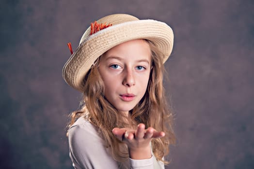 nice girl with blond hair in white dress and straw hat blowing over the hand