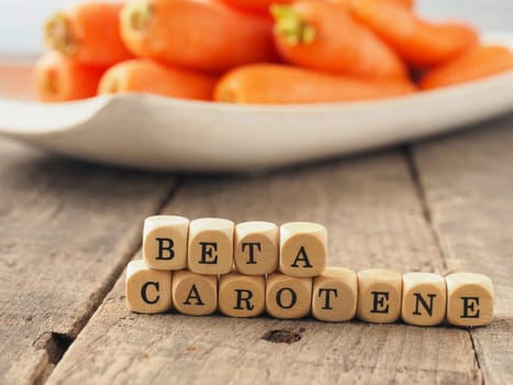 Wooden dices with the words beta carotene and fresh carrots in the back, healthy eating concept