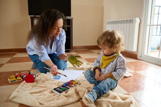 Mother and child share a joyful moment painting together on the floor. Capturing maternal bonding and creativity in a warm, relaxed atmosphere.