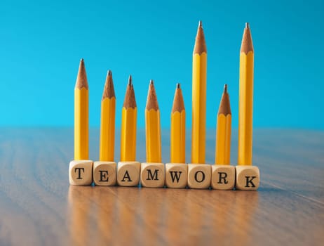 Teamwork concept with a row of yellow pencils and wooden dices with the word teamwork on an office table