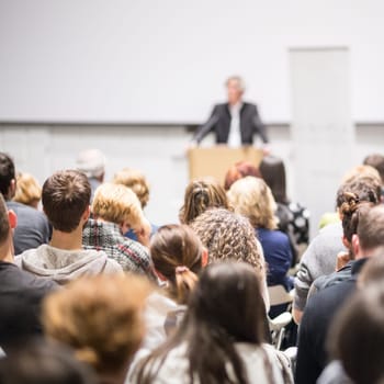 Speaker giving a talk in conference hall at business event. Audience at the conference hall. Business and Entrepreneurship concept. Focus on unrecognizable people in audience.