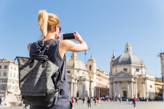 Female tourist with a fashinable vintage hipster backpack taking photo of Piazza del Popolo, People's Square, in Rome, Italy by her mobile phone.