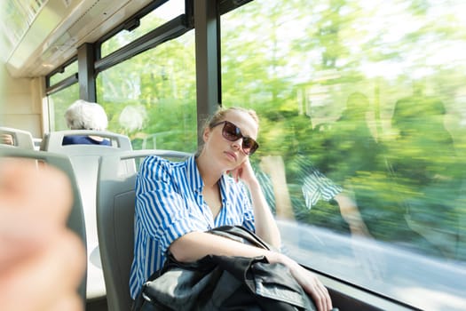 Portrait of woman sleeping on moving bus by window. Tired passenger sleeps on long countryside bus ride home.