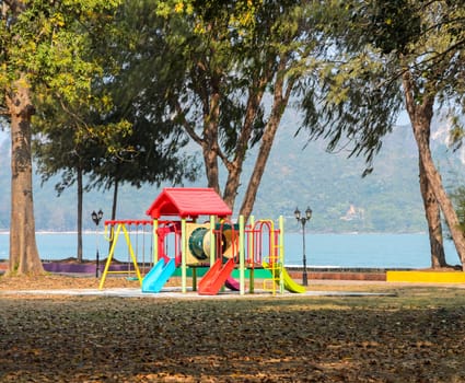 Colorful childrens playground near the sea, mountain on background. Plastic slides and climbers in public park