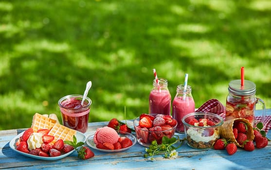 Fresh, healthy, vibrant summer strawberry smoothie bowl, juices and desserts picnic on a bright outdoor table setting.