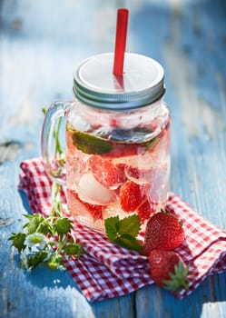 Fresh, chilled fruit and berry infused punch in a glass jar with a straw on a bright outdoor table setting.