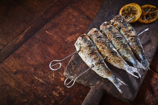 Grilled fish on skewers served on rustic wooden table viewed in close-up from above with copy space
