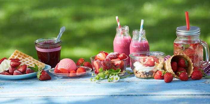 Fresh, healthy, vibrant summer strawberry smoothie bowl, juices and desserts picnic on a bright outdoor table setting.