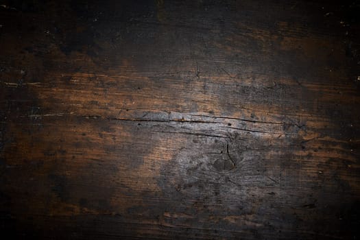 Old dark aged blackened burnt wood background texture with cracks and surrounding vignette