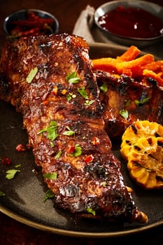 Delicious seasoned spicy portion of barbecued spare ribs with chili and herbs served with roasted corn and potato chips in a close up view on a plate